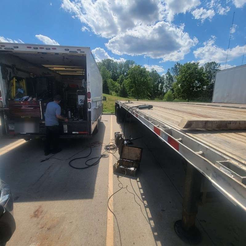 Mobile mechanic working from a fully stocked service truck beside a flatbed trailer