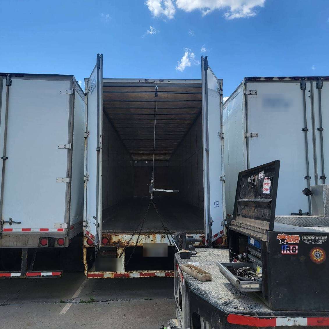 Reefer trailer doors open for repair, service truck parked alongside in the yard